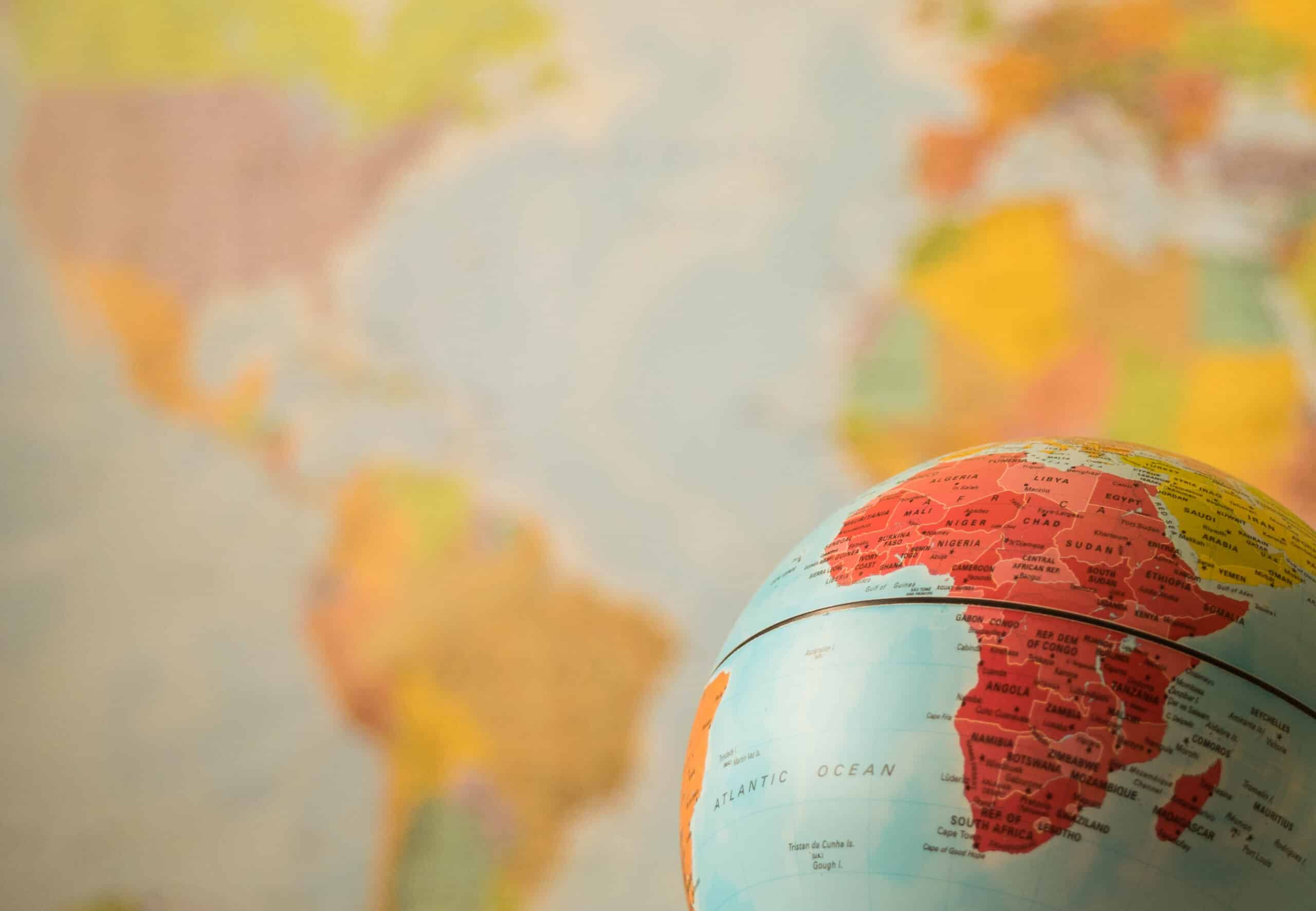 A photo of a colourful globe in the foreground of the picture. The image is focusing on Africa. The background is covered by a map.